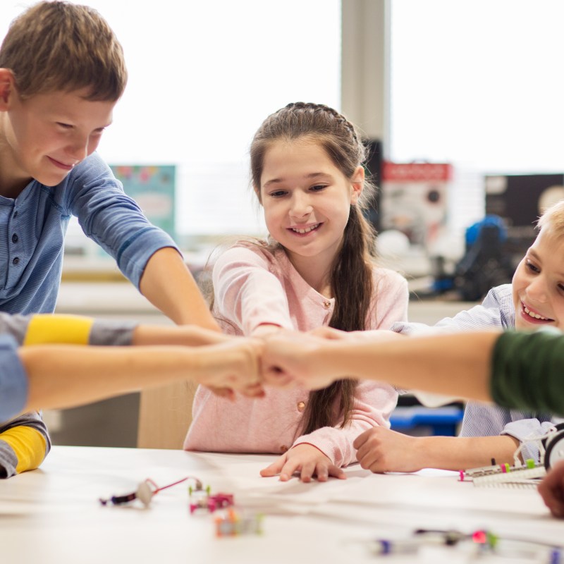 Smiling children in a classroom giving a group fist bump over a table.