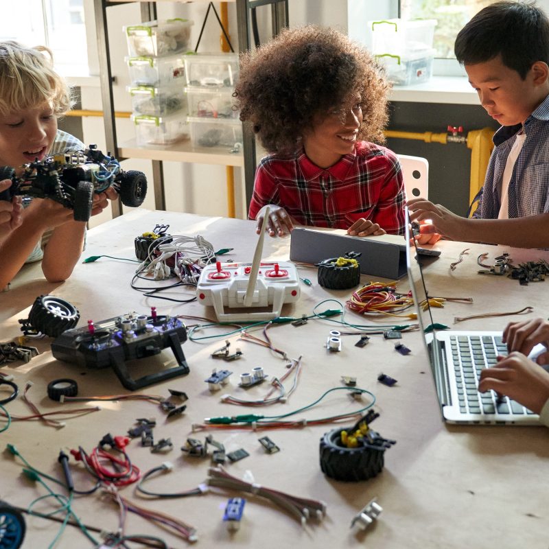 Children collaborating on electronics projects at a table with laptops and components.